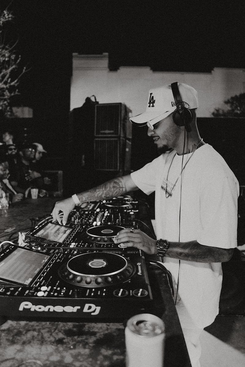 Black and white photo of DJ mixing music on deck outdoors at night.